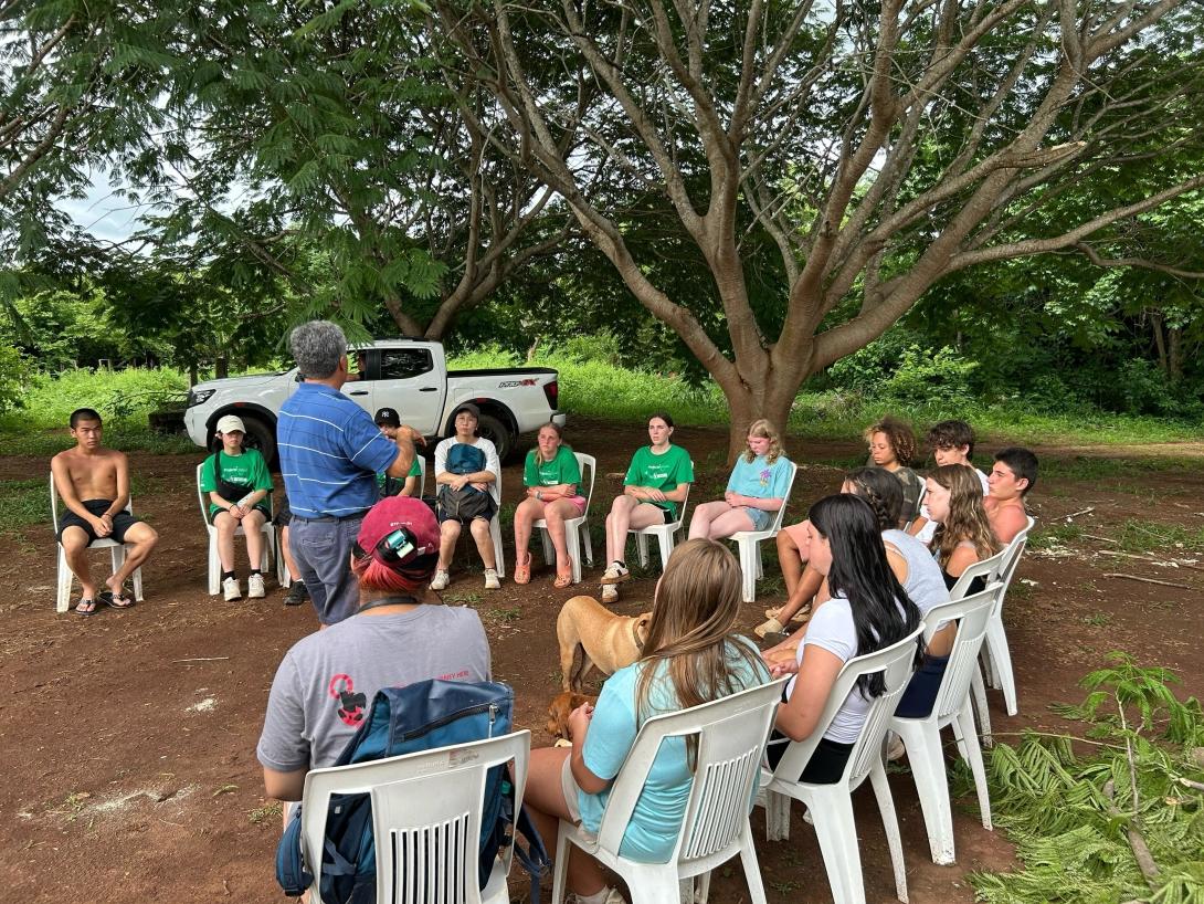 Group of conservation volunteers sitting in circle while placement supervisor gives instructions 